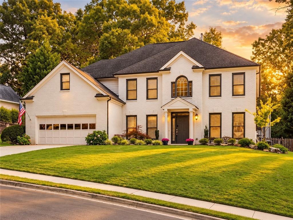 Two-story white brick home with an attached garage and broad front lawn at sunset.