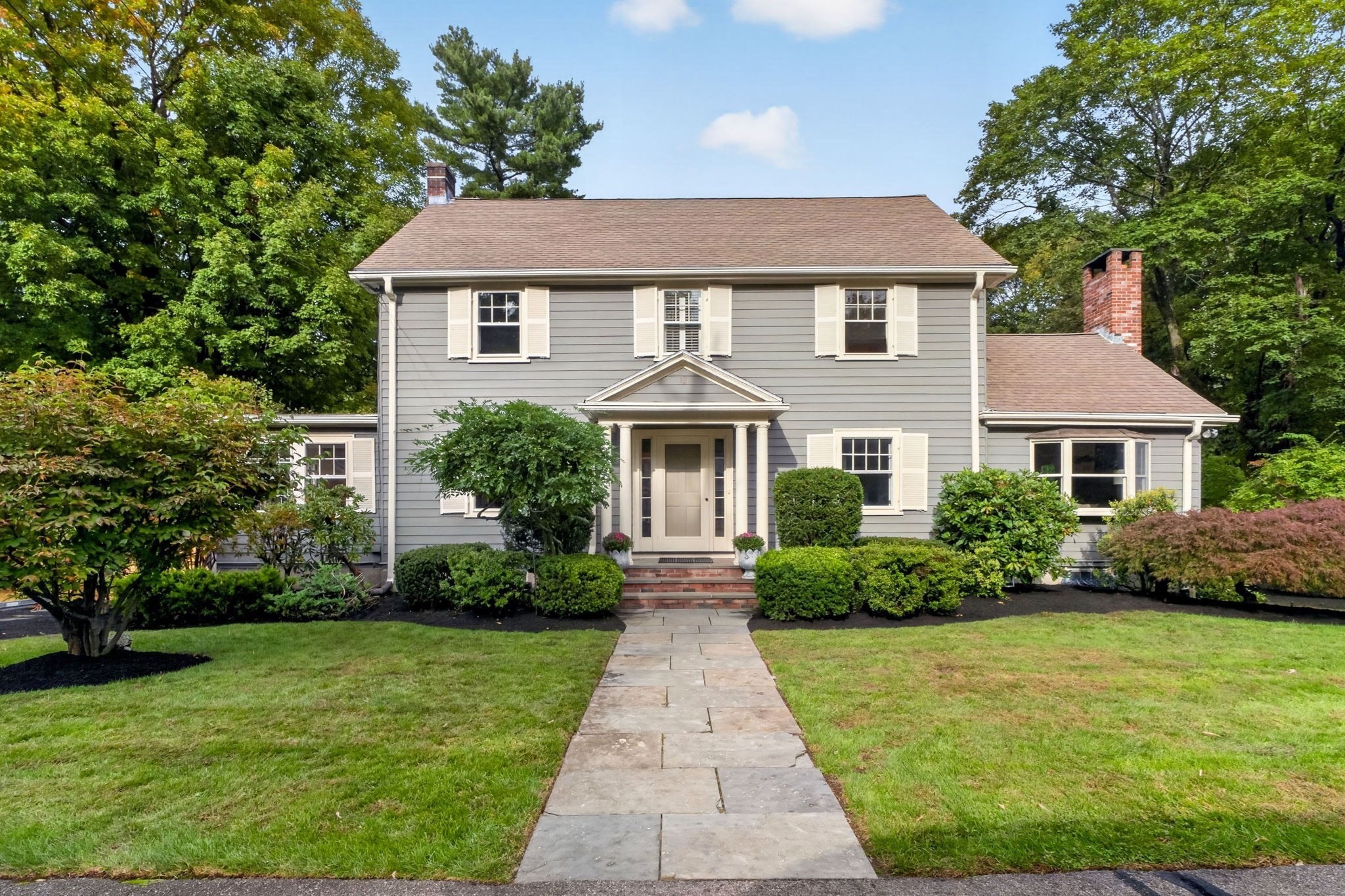 Gray two-story home with a columned entrance, brick chimneys, and a stone walkway through the front yard.