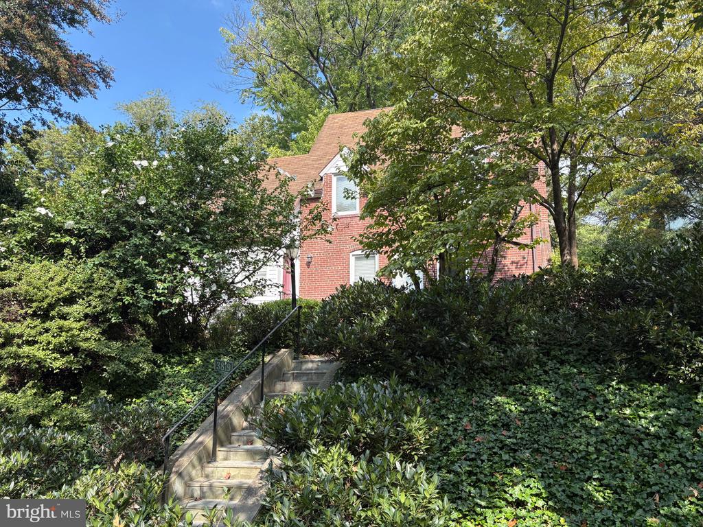 Red-brick two-story house partly hidden by trees, above landscaped steps with a handrail.