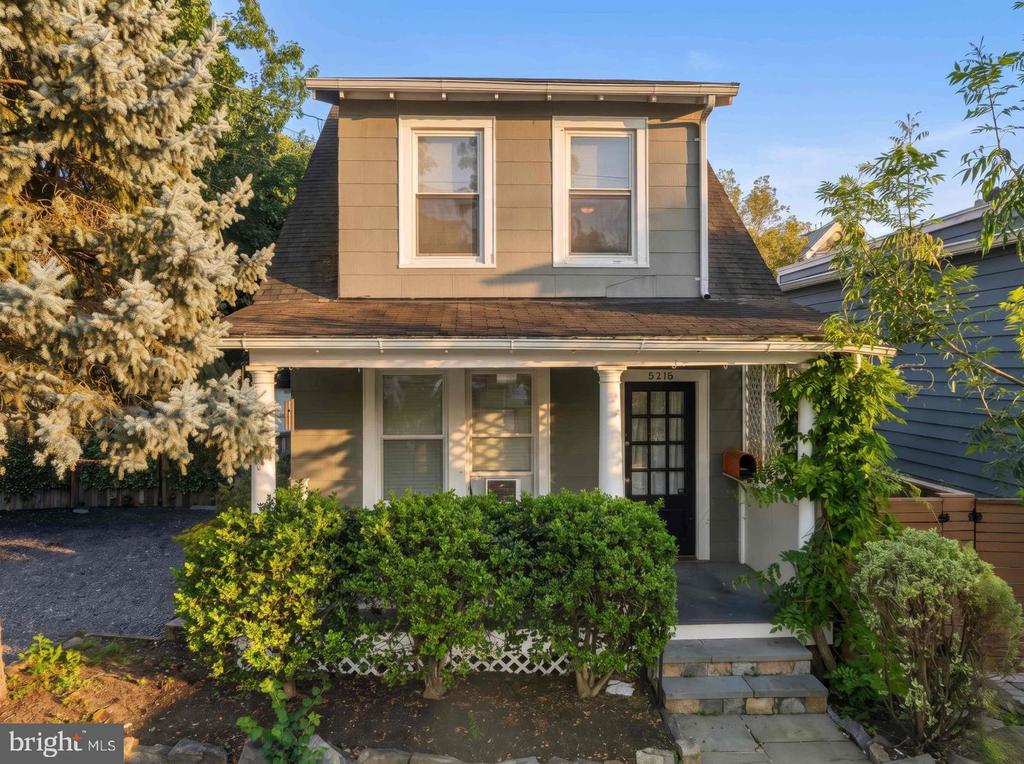 Two-story house with a covered porch, black front door, and mature trees.