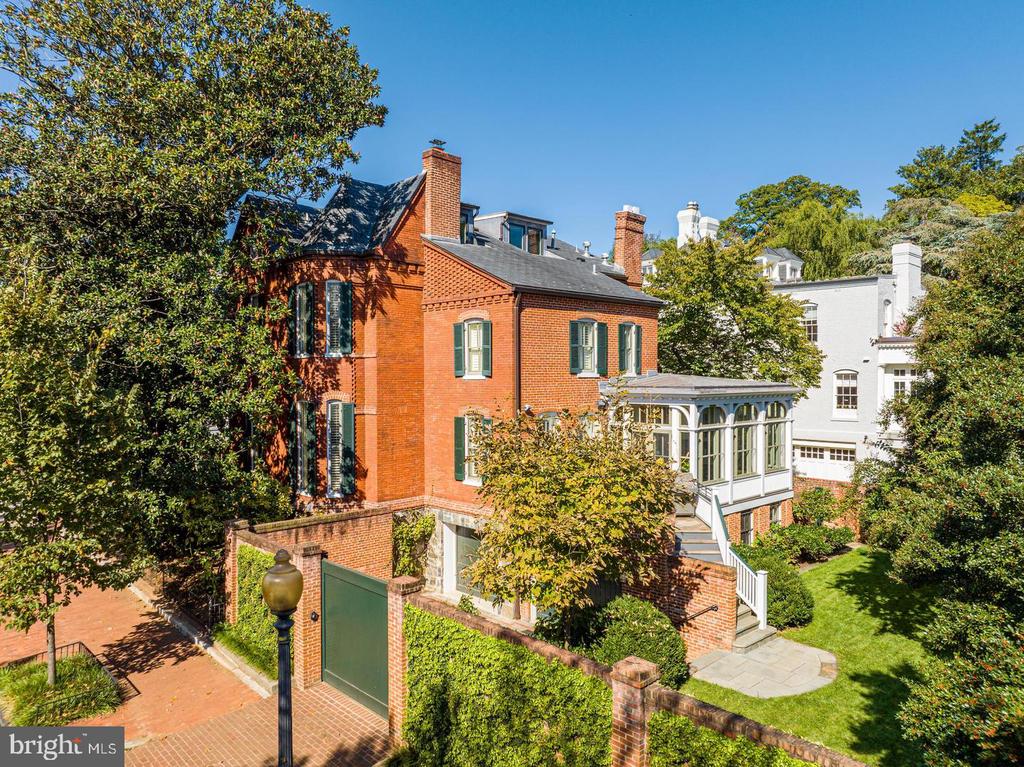 Red-brick townhouse with green shutters and a glass-enclosed porch, surrounded by leafy landscaping.
