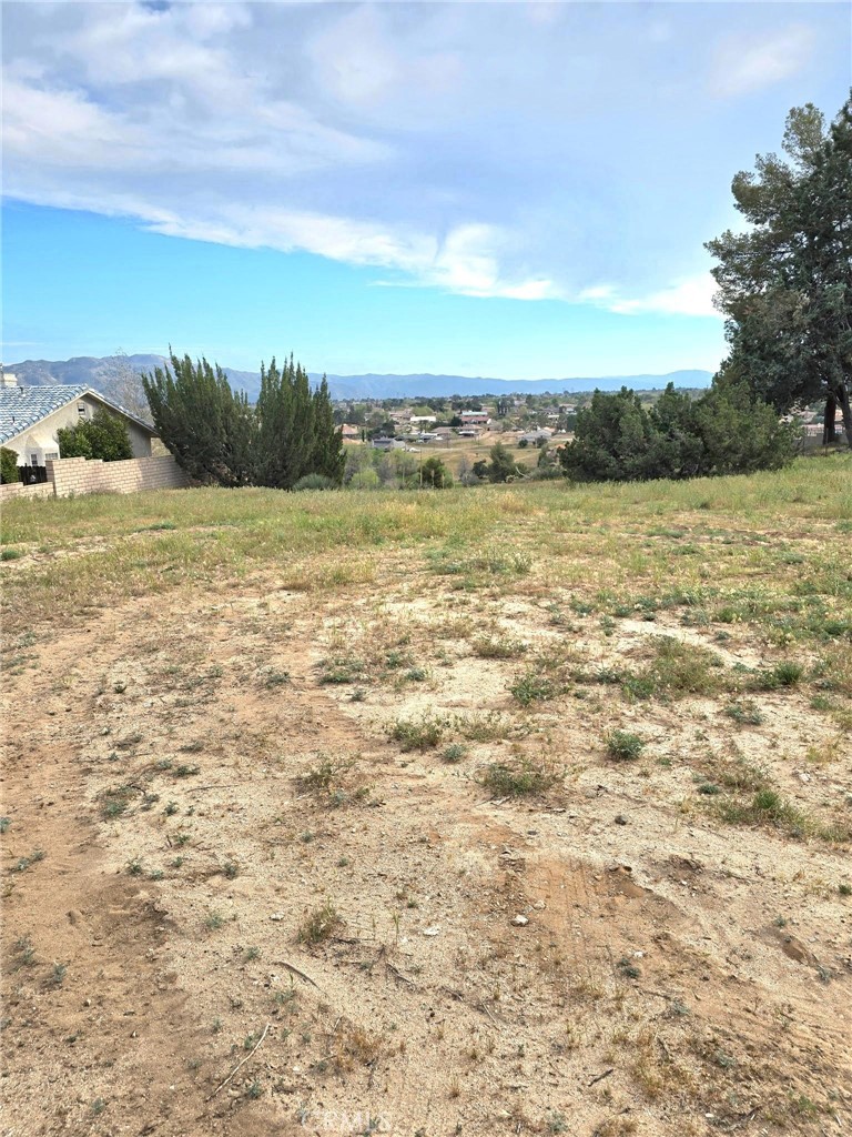 Vacant dry lot with sparse grass, neighboring homes, and distant mountain views.