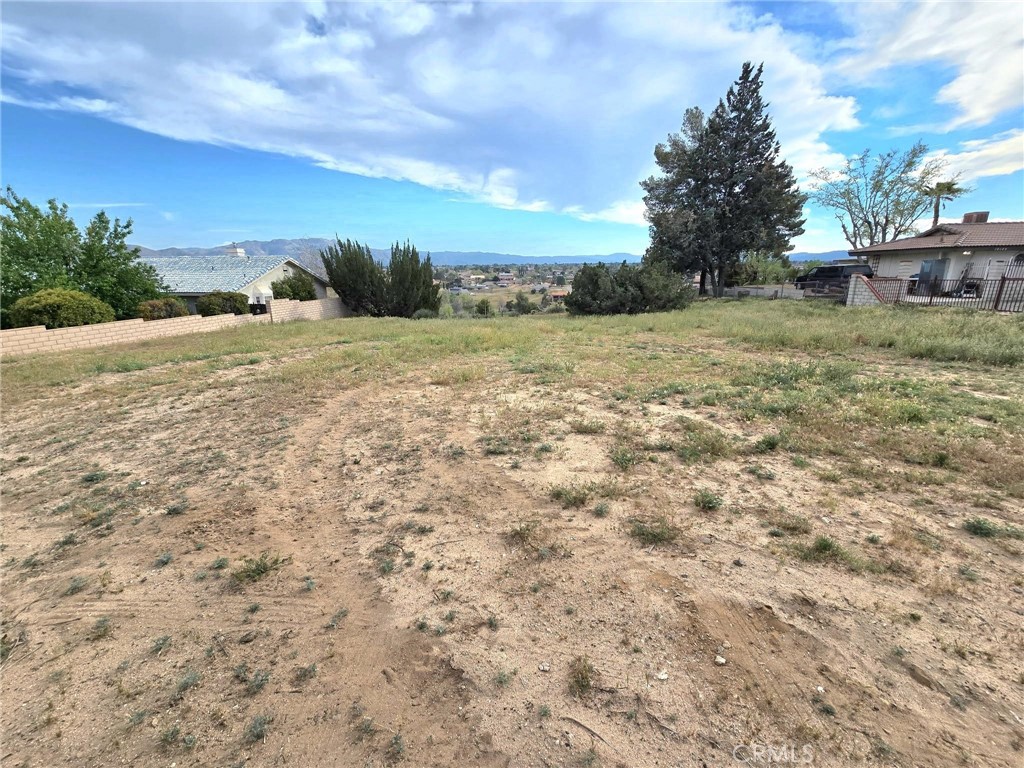 Vacant lot with dry, uneven ground, neighboring homes, and distant mountain views.
