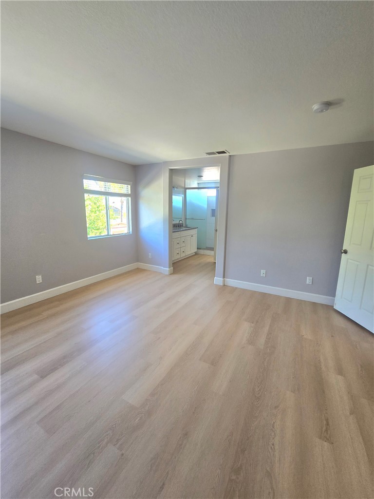 Empty bedroom with light wood-look flooring and an open doorway to the bathroom.