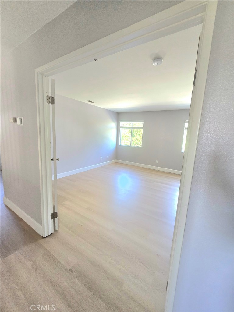 Empty, sunlit room with pale wood floors, gray walls, and windows.