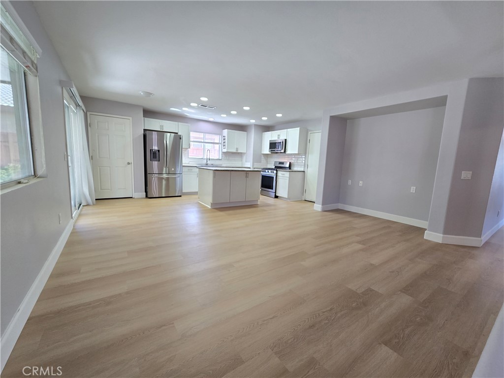 Open kitchen and living area with a white island, stainless steel appliances, and light wood-look flooring.
