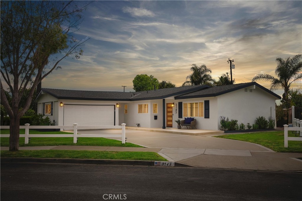 Single-story home with an attached garage, white fence, and front lawn at dusk.