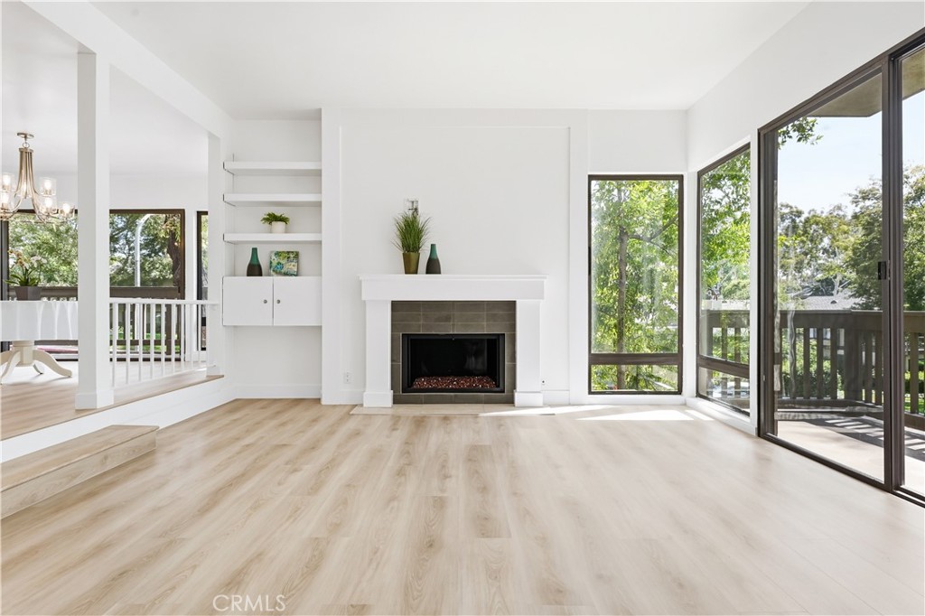 Bright living room with a white fireplace, pale wood floors, and large glass doors to a deck.