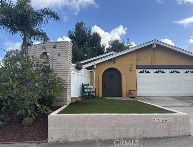Single-story home with an arched front door, double garage, and low concrete yard wall.