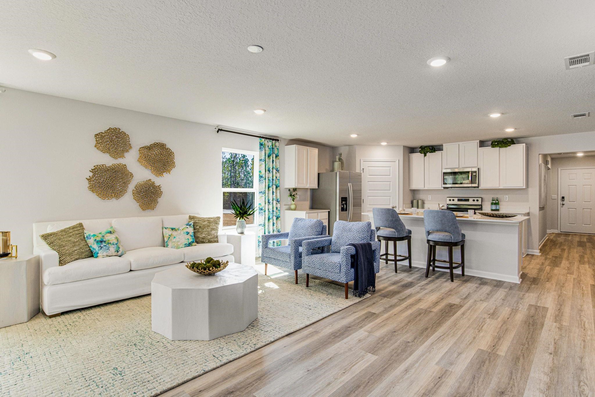 Open-plan living room and kitchen with a white sofa, blue armchairs, and breakfast bar.