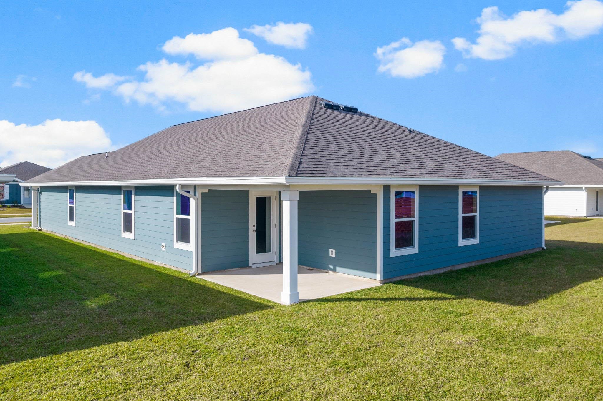 Blue single-story house with white trim and a small concrete patio beside a broad lawn.
