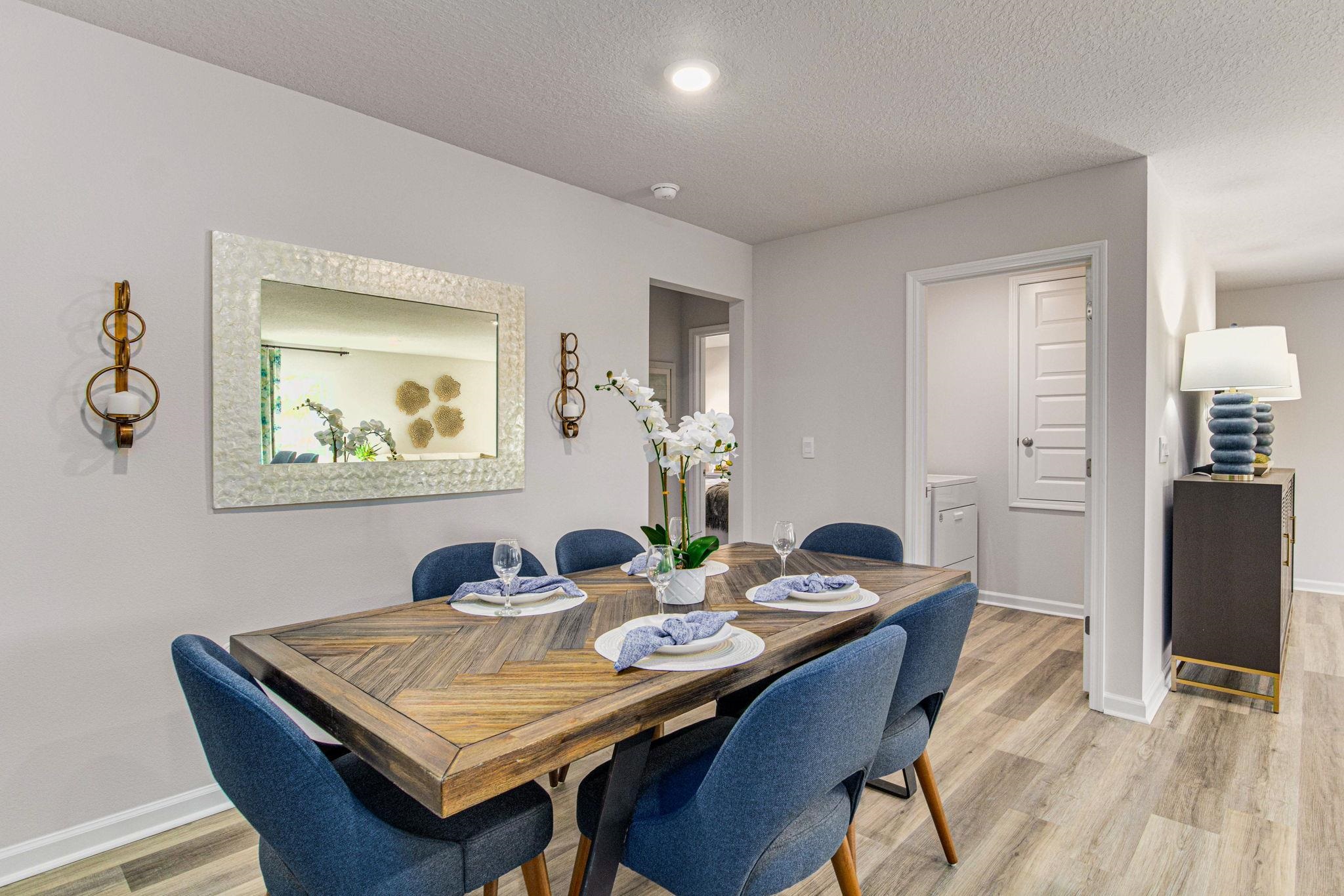 Staged dining room with a rustic wood table, blue chairs, and white orchids.