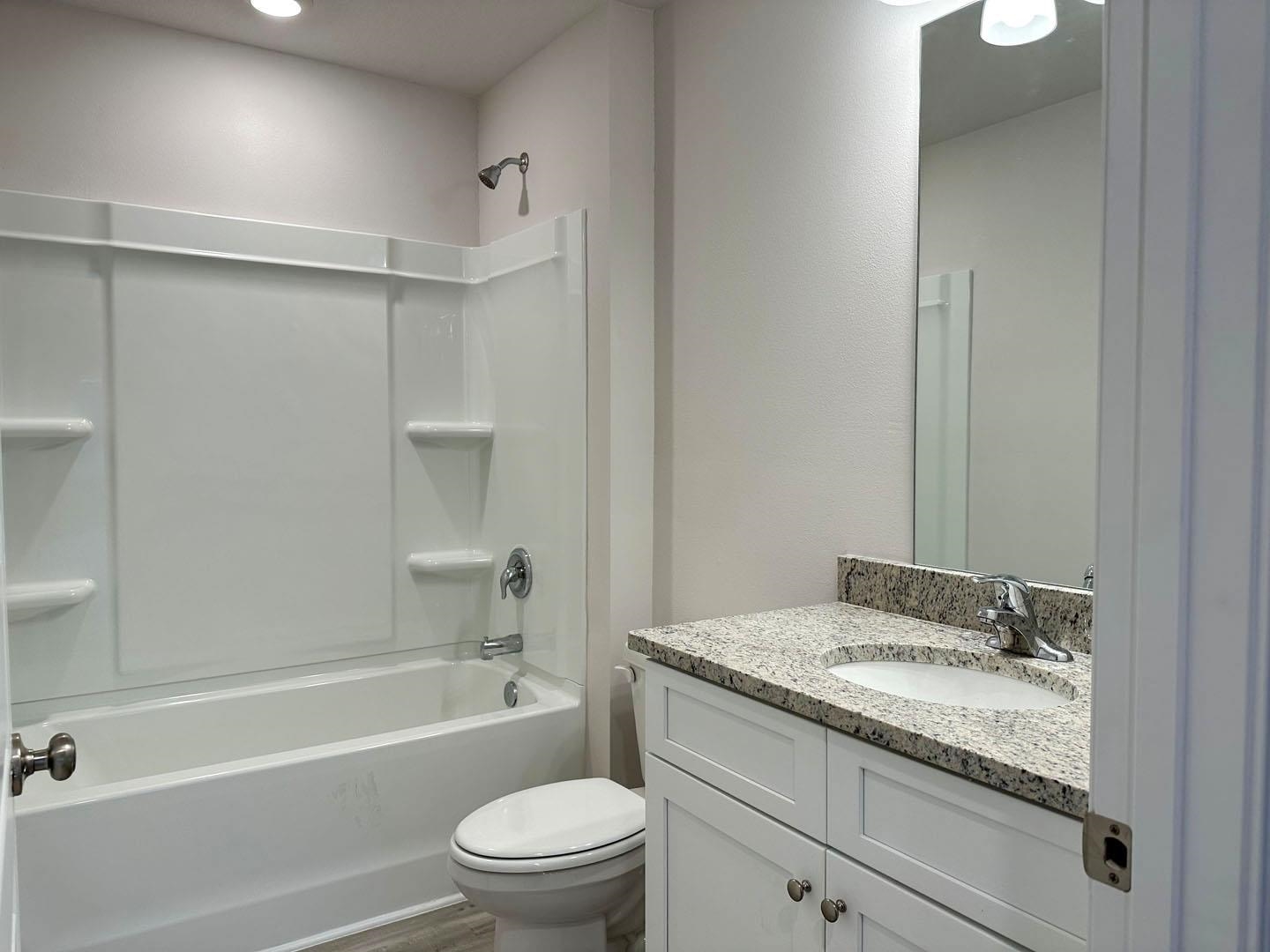 Bathroom with a white tub-shower and granite-topped vanity with an oval sink.