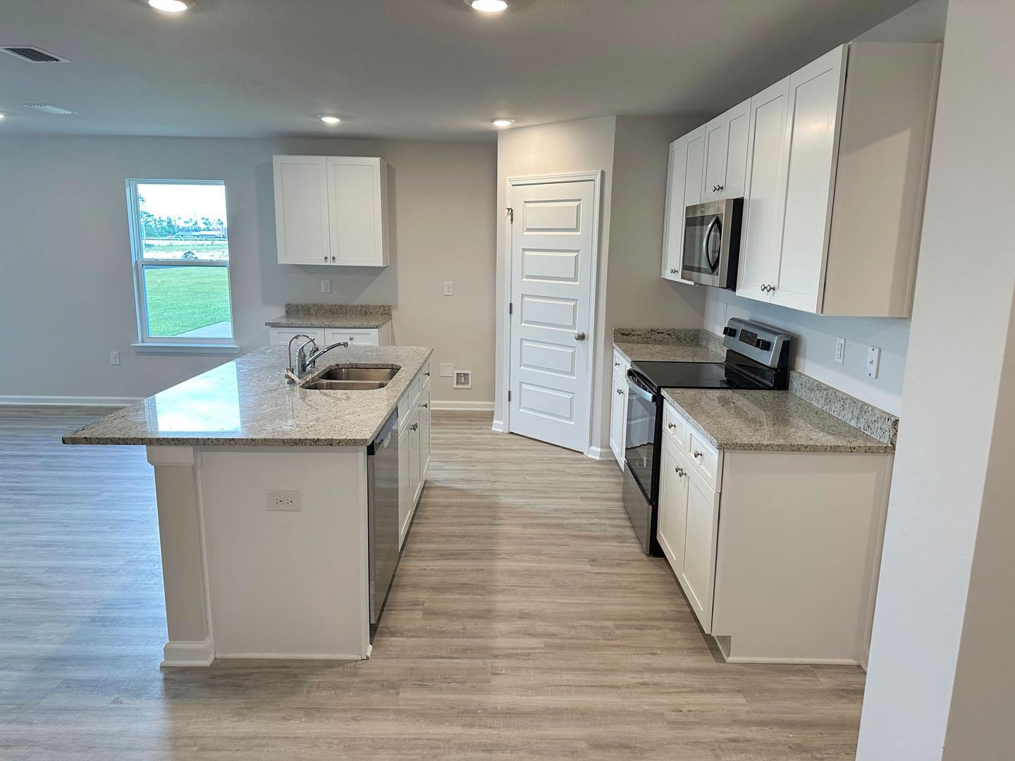 Vacant kitchen with white cabinets, granite island and double sink, and stainless steel appliances.