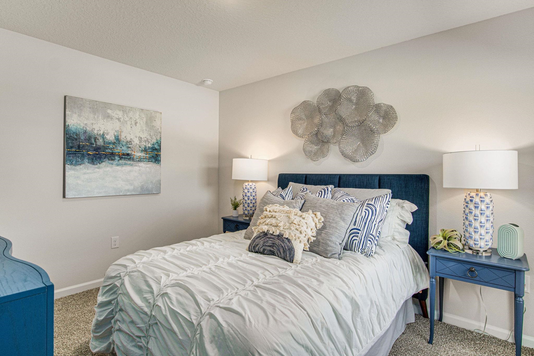 Staged bedroom with a white quilted bed, blue headboard, matching nightstands, and abstract wall art.
