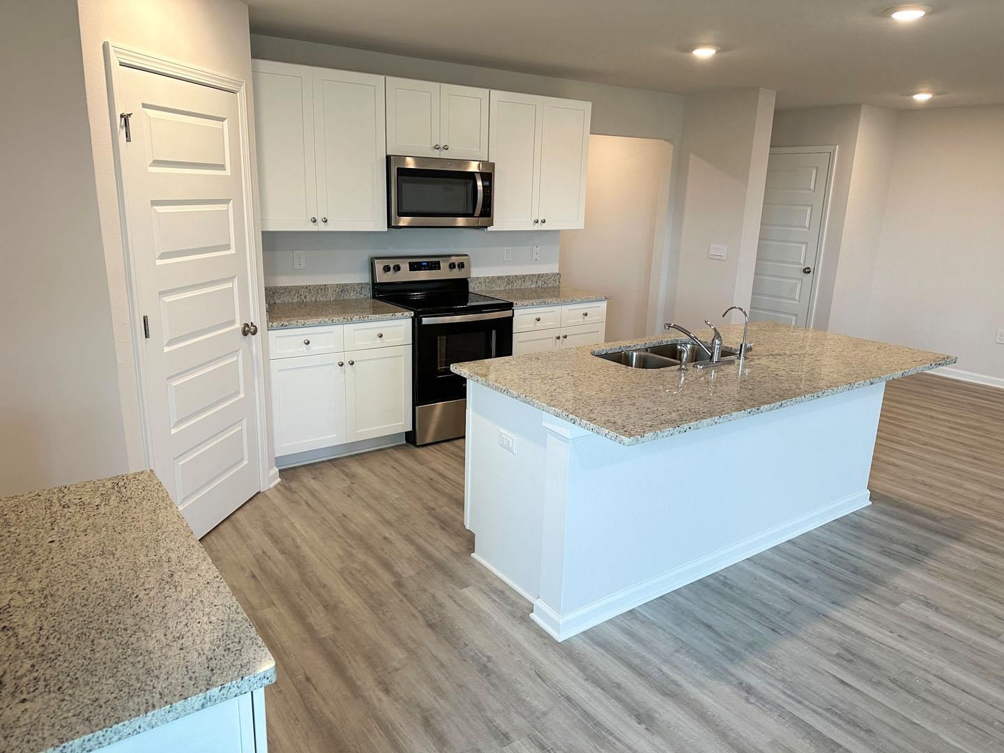 Kitchen with a large granite island, white cabinetry, stainless steel appliances, and wood-look flooring.