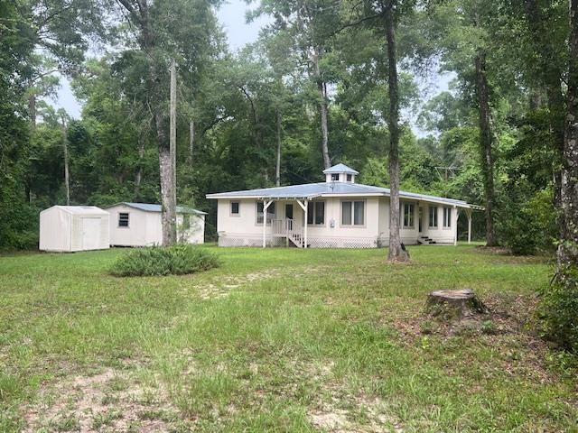 Single-story house with a covered porch and roof cupola in a wooded clearing, with a detached outbuilding.