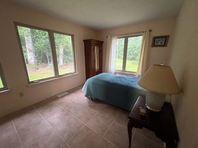 Bedroom with a blue-covered bed, tiled floor, and windows overlooking trees and lawn.