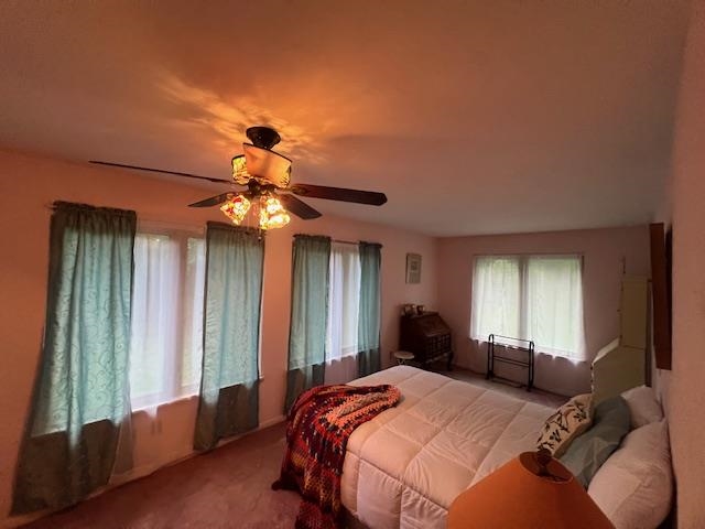 Furnished bedroom with teal window curtains, a colorful bed throw, and a lit ceiling fan.