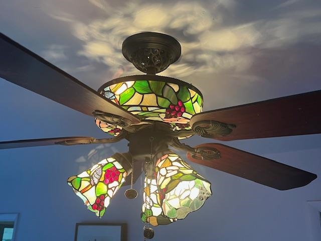 Ceiling fan with colorful stained-glass light shades against a blue ceiling.