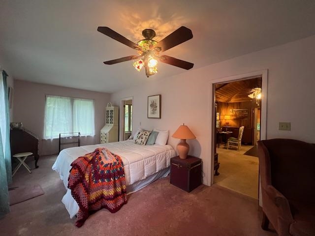 Furnished bedroom with a colorful quilt, ceiling fan, and doorway to a wood-paneled room.