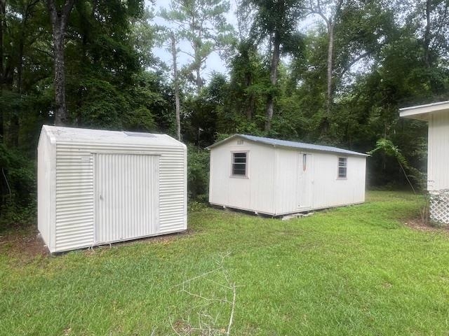 Two white storage sheds in a grassy, tree-lined yard.