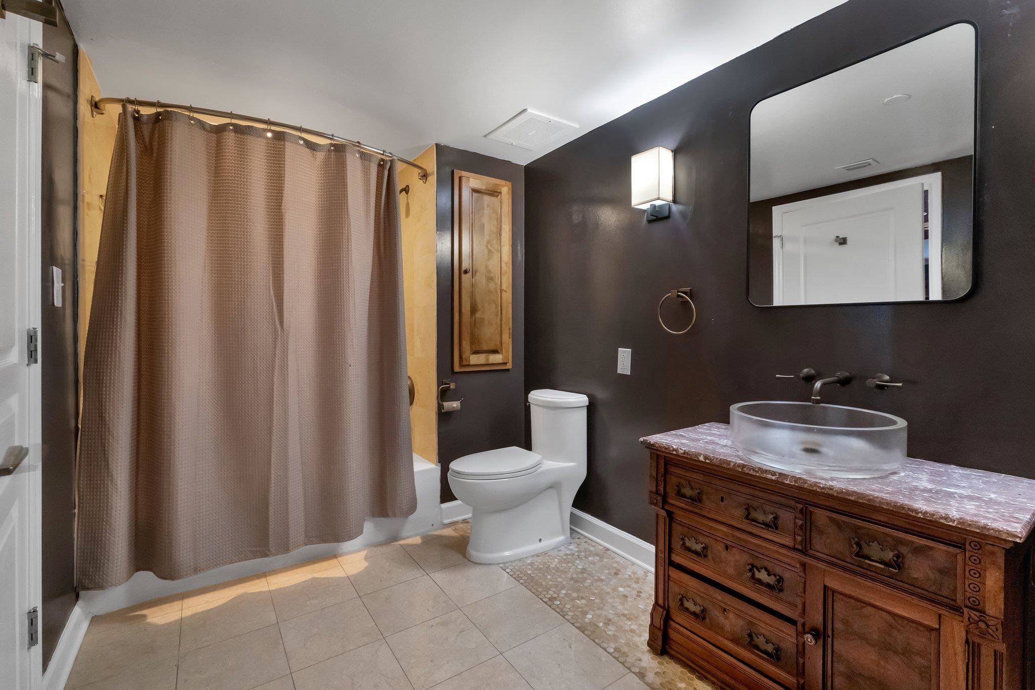 Bathroom with a glass vessel sink, ornate wooden vanity, dark walls, and a curtained tub and shower.