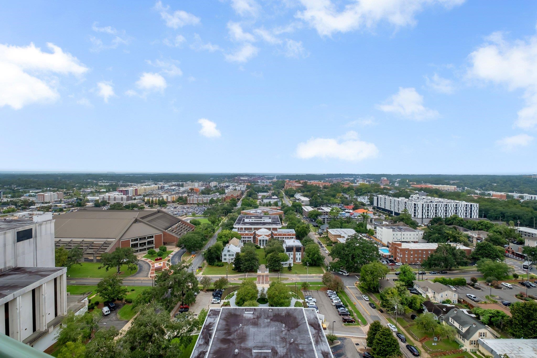 Aerial view of downtown Tallahassee, with city buildings, tree-lined streets, and a broad blue sky.