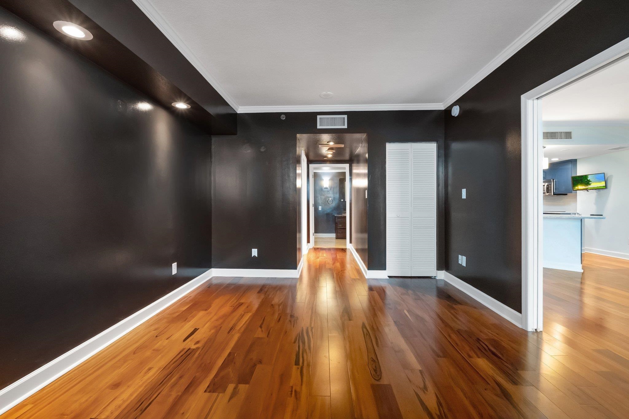 Empty condo living area with dark walls, hardwood floors, and an open doorway to the kitchen.