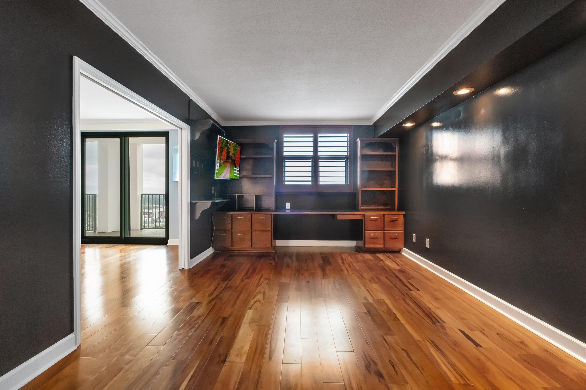 Home office with built-in wooden desk, shuttered windows, and hardwood floors beside a balcony door.