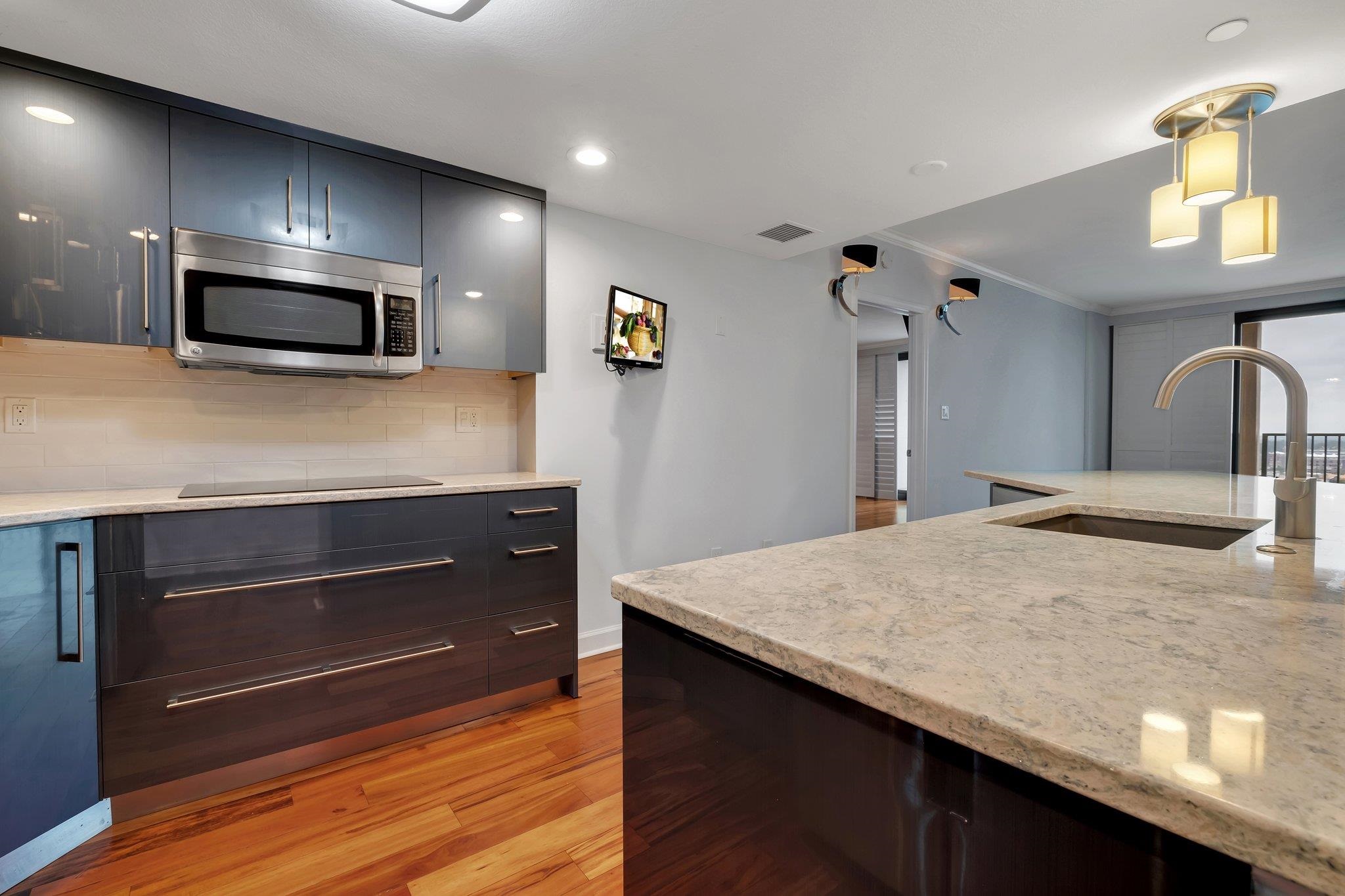 Modern kitchen with dark cabinetry, stone island, integrated sink, and warm hardwood floors.