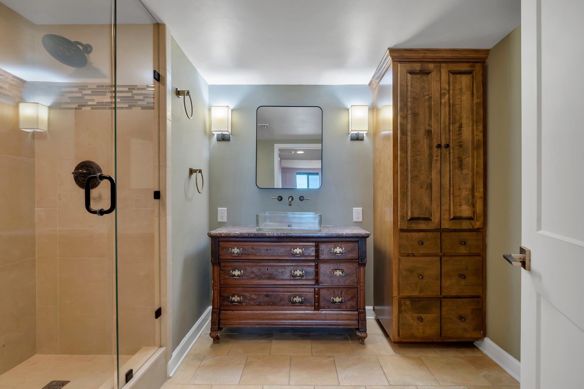 Bathroom with a glass-enclosed shower, dark wood vanity, vessel sink, and tall matching cabinet.