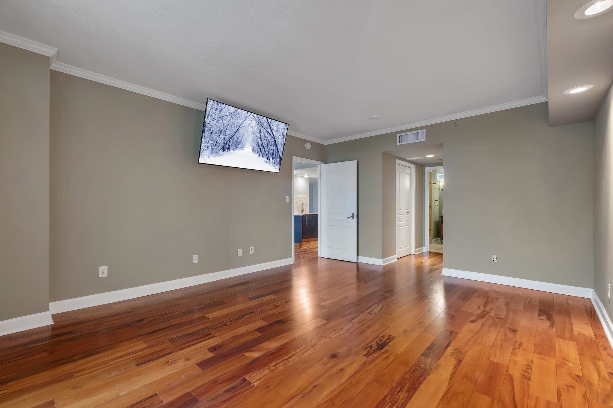Mostly empty living room with warm hardwood floors and a wall-mounted television.