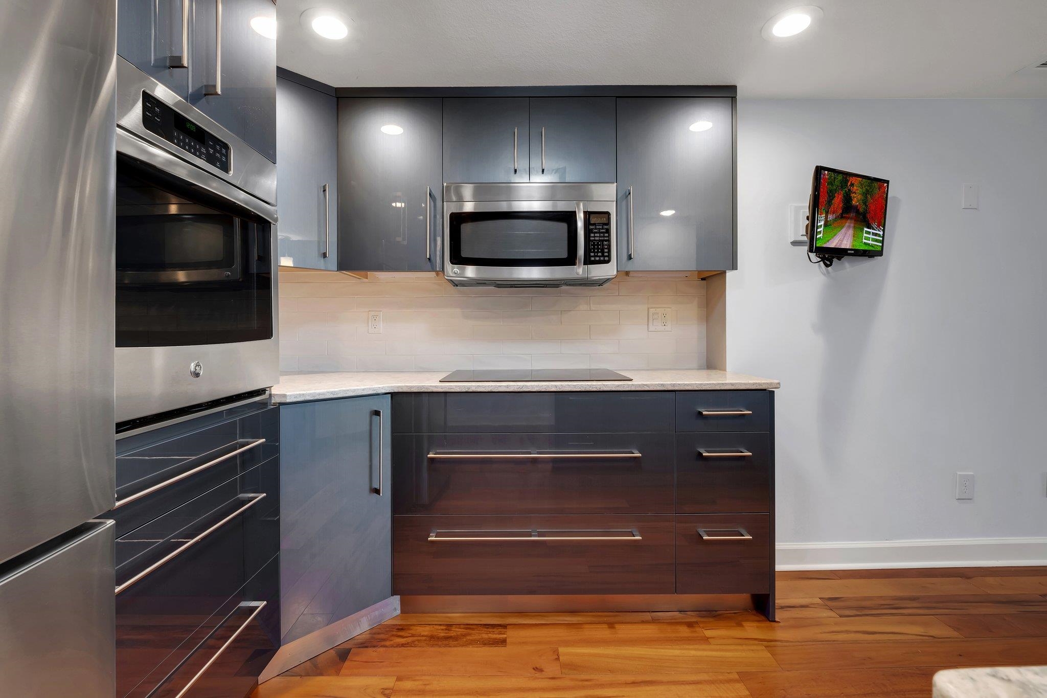 Modern condo kitchen with dark cabinets, stainless steel appliances, and a wall-mounted television.