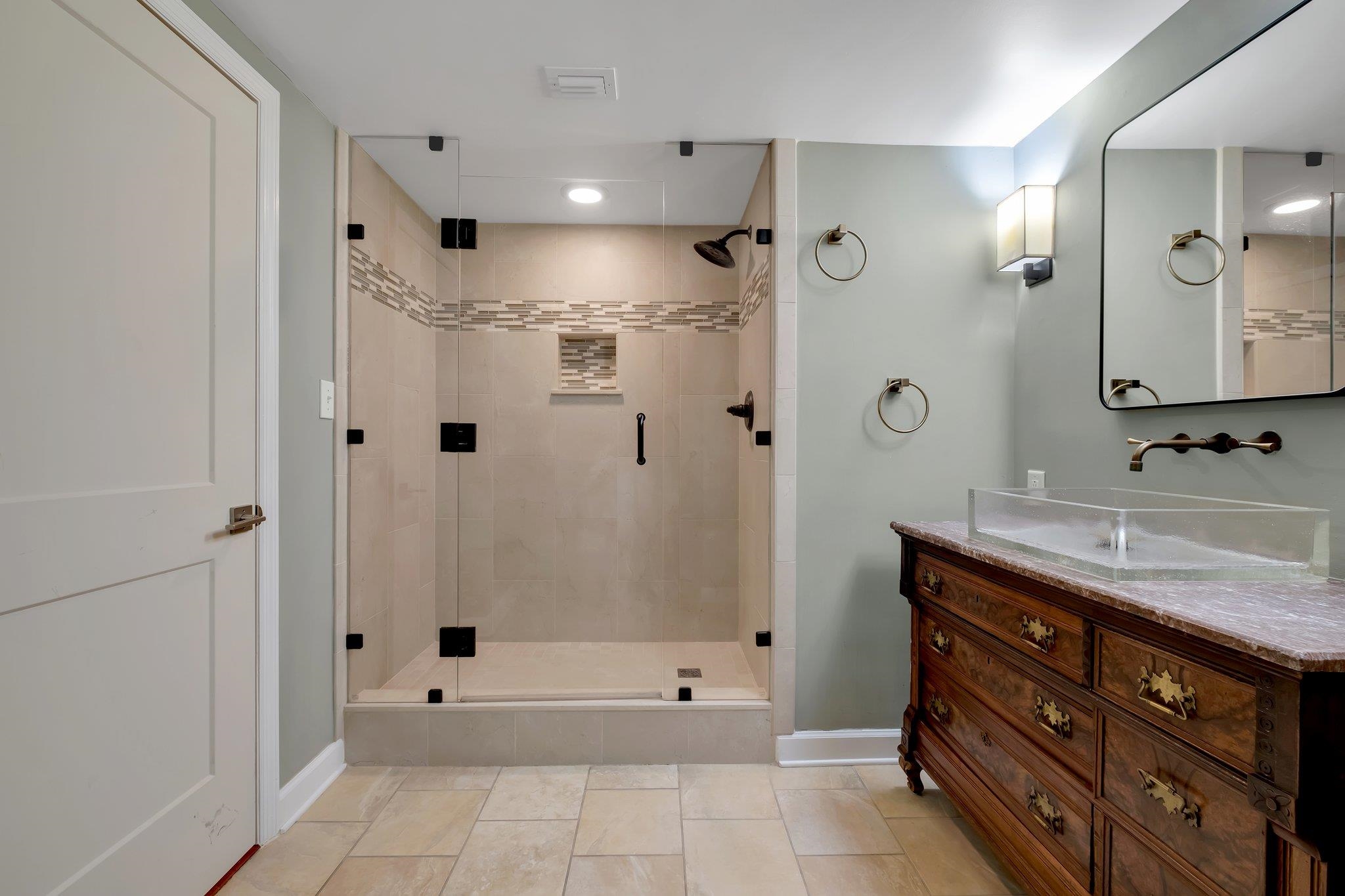 Bathroom with a glass-enclosed tiled shower and ornate wood vanity with a glass vessel sink.