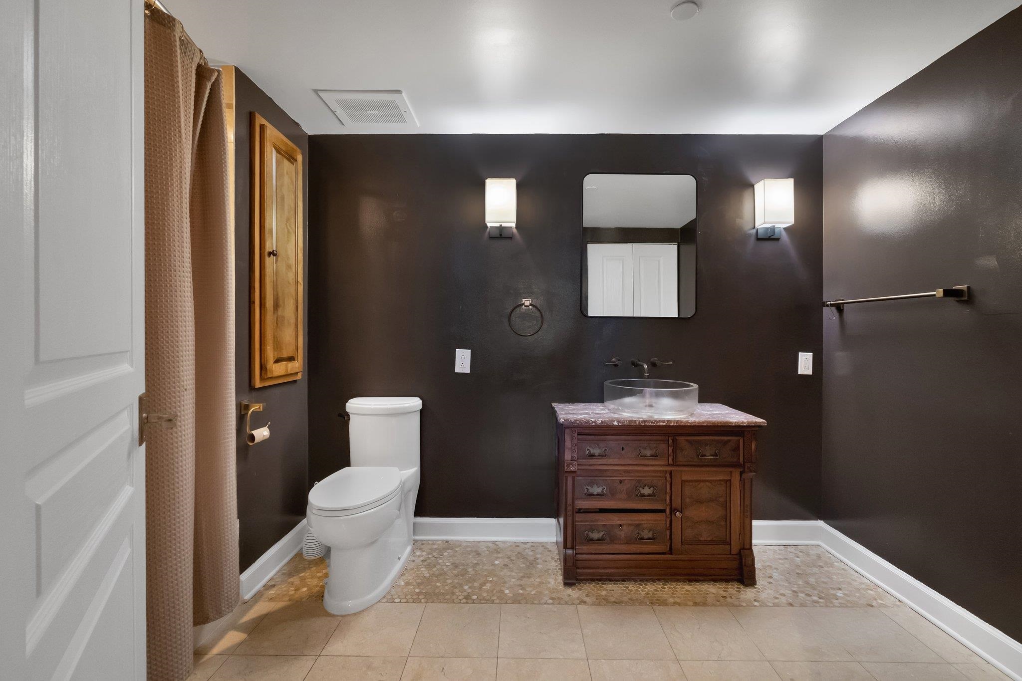 Bathroom with dark walls, a rustic wooden vanity, vessel sink, and white toilet.