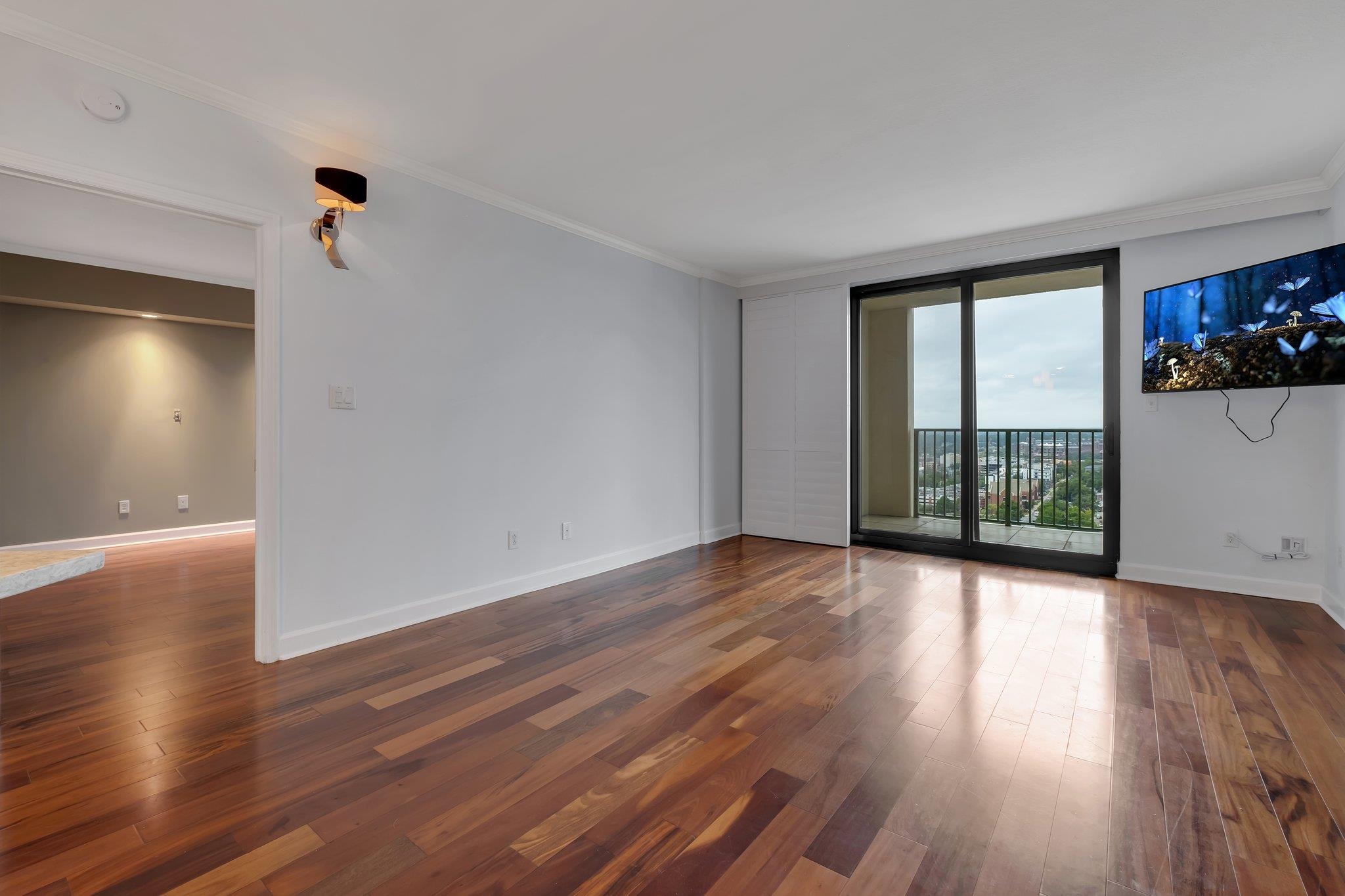 Empty living room with hardwood floors and sliding balcony doors overlooking the city.
