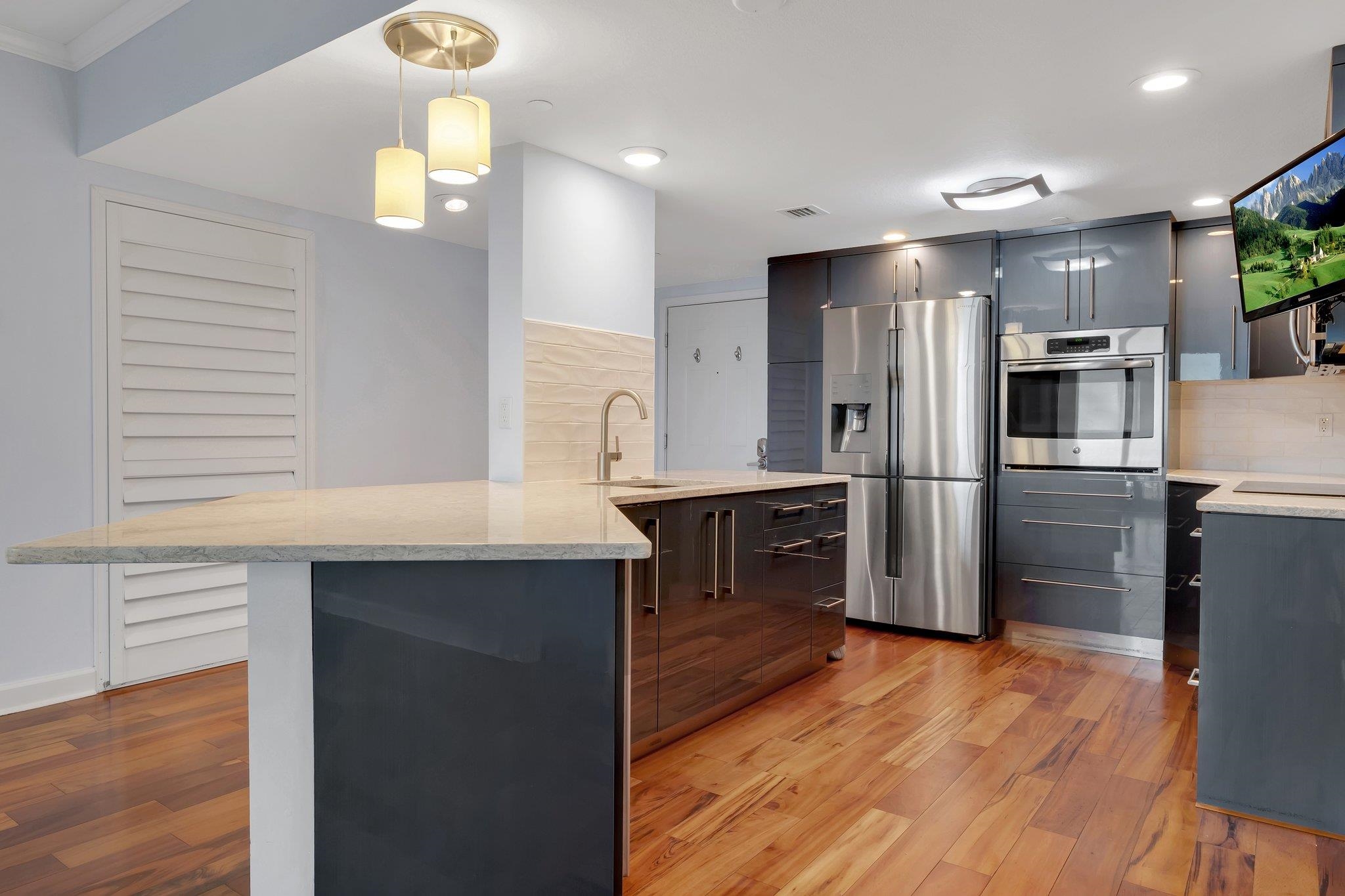 Modern kitchen with a broad stone island, dark cabinets, stainless steel appliances, and wood floors.