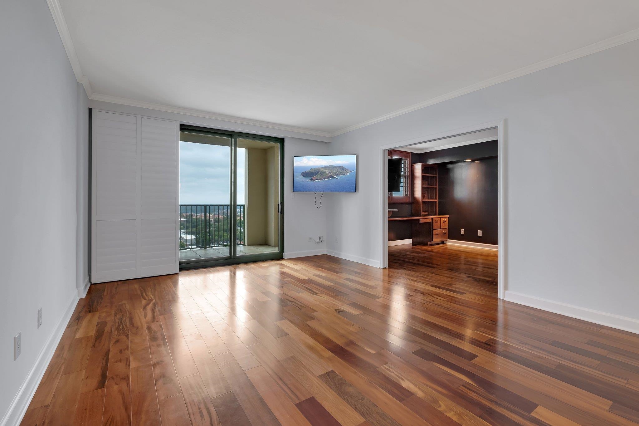 Unfurnished condo living room with wood floors, balcony doors, and an adjoining room with dark built-in cabinetry.