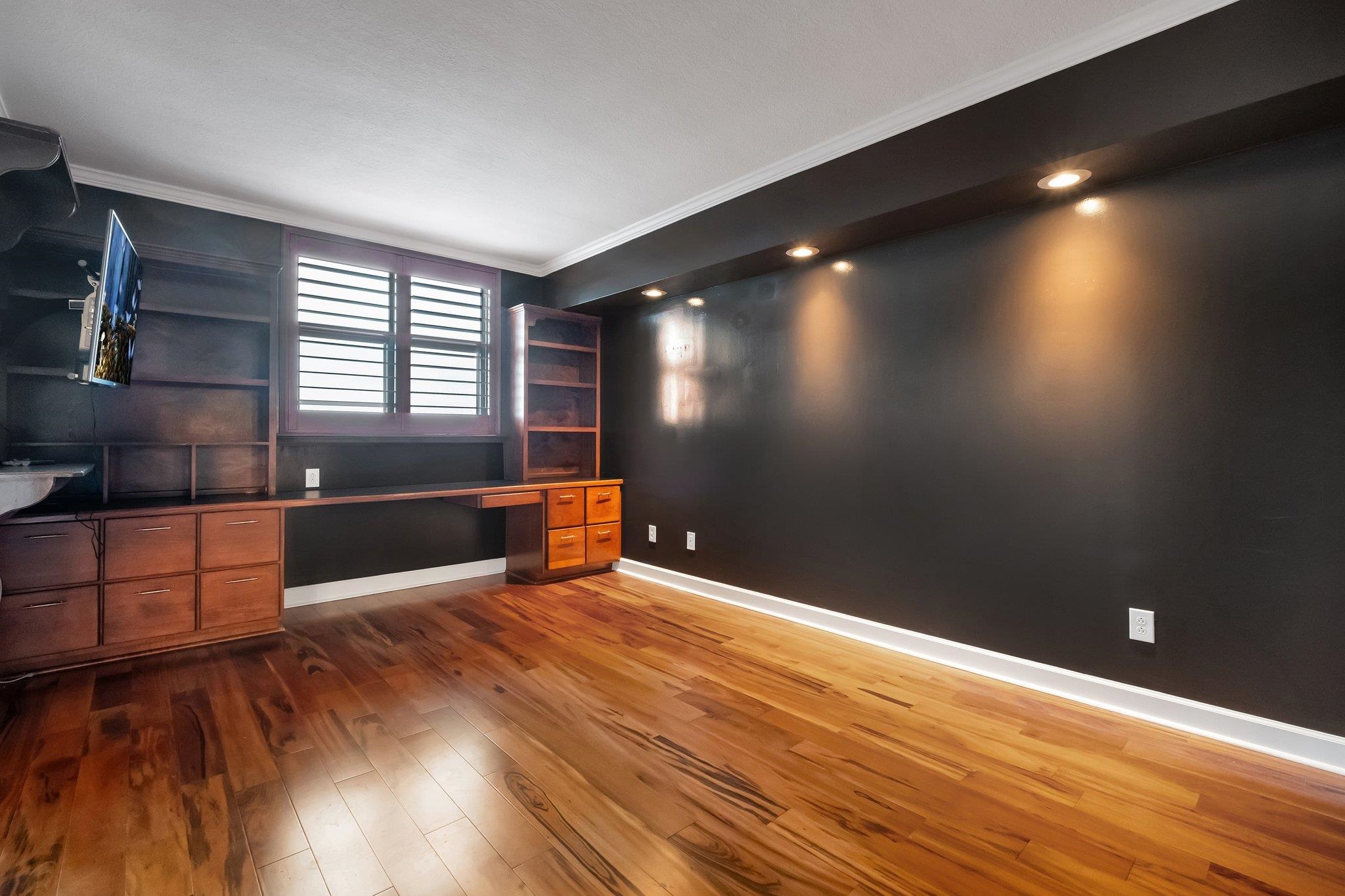 Office with built-in wooden desk and shelving, shuttered windows, and hardwood floors.