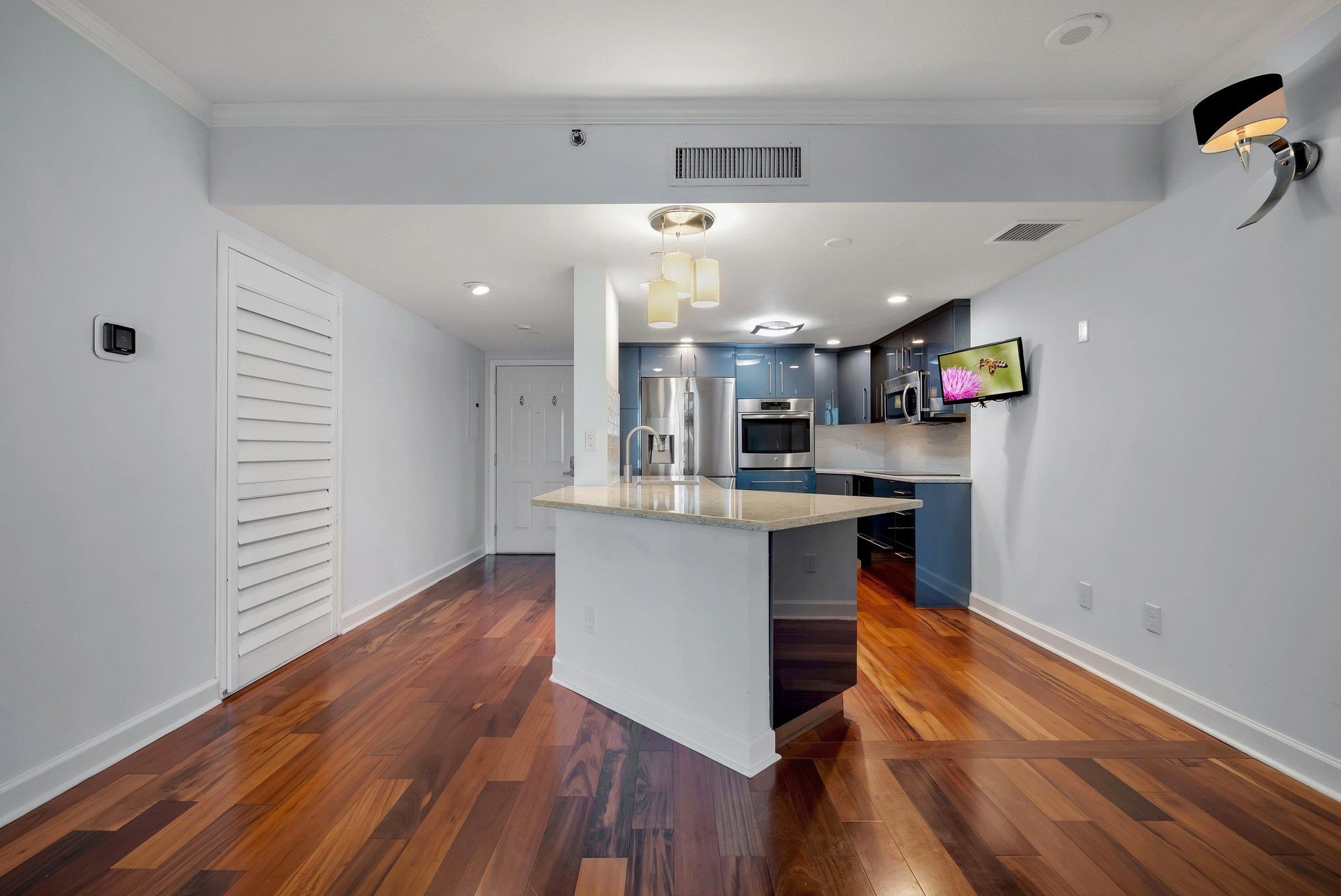 Condominium kitchen with blue cabinets, stainless appliances, a stone island, and wood floors.