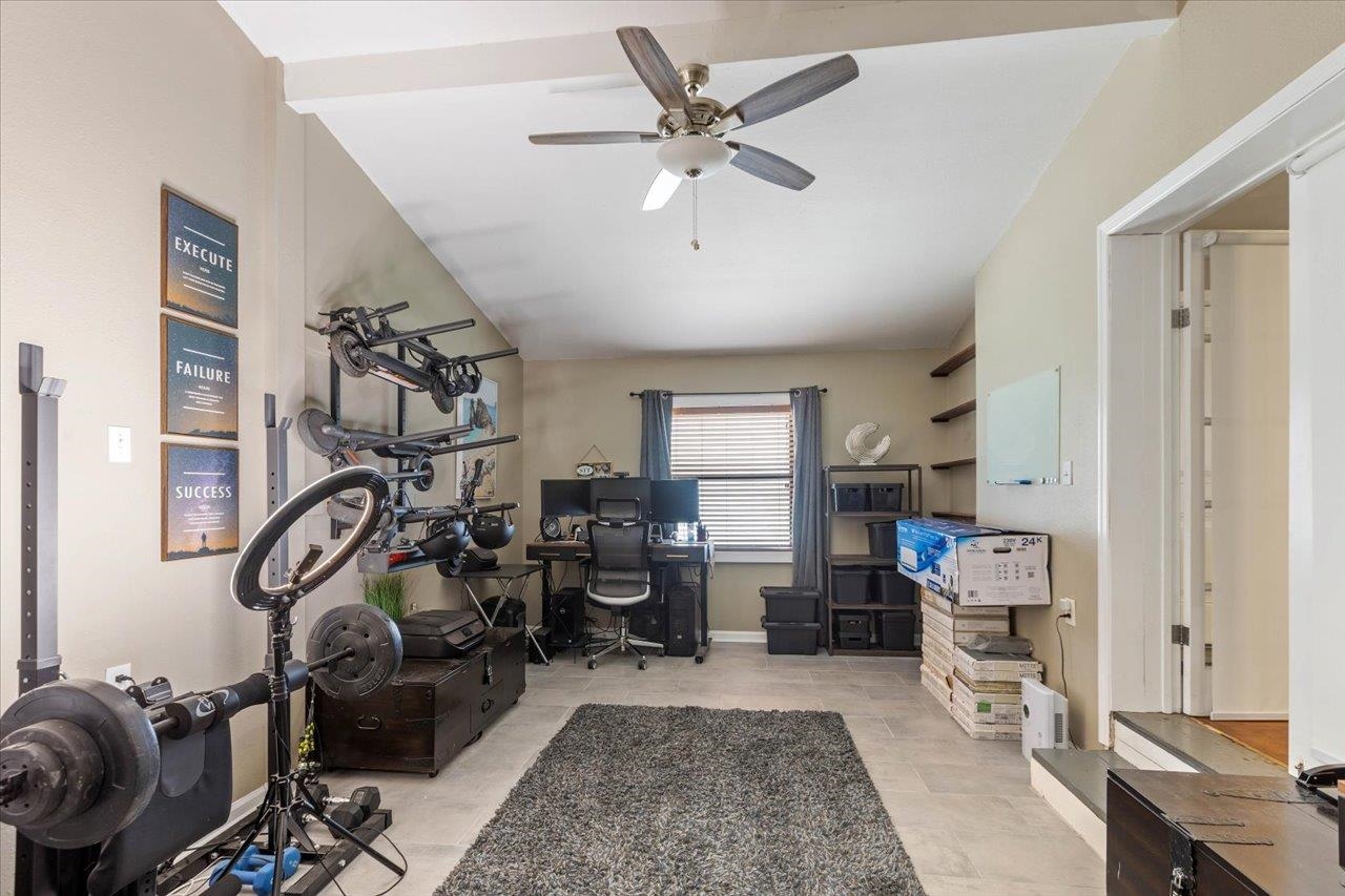 Home gym and office with exercise equipment, a desk by the window, and storage shelves.