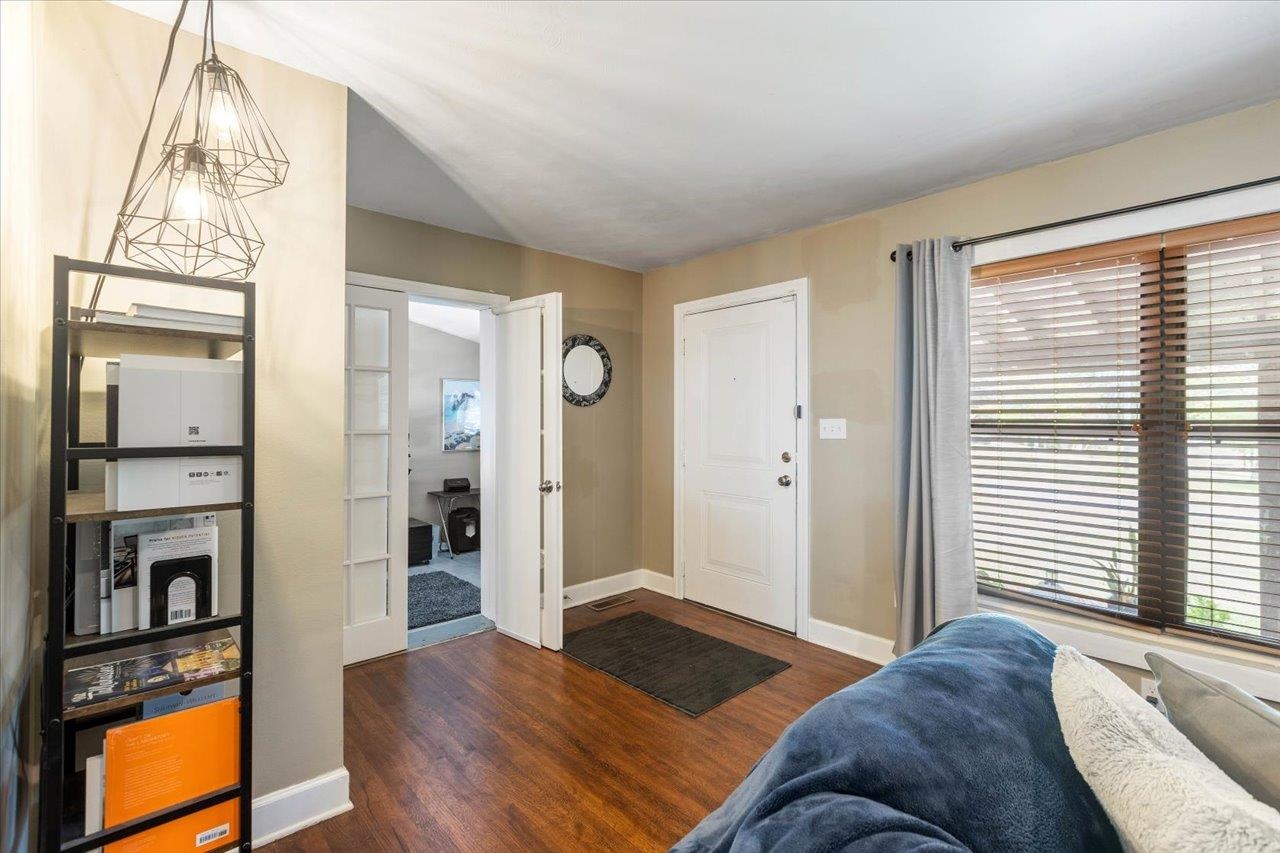 Living room and entry with hardwood floors, a white front door, wide window, and blue sofa.