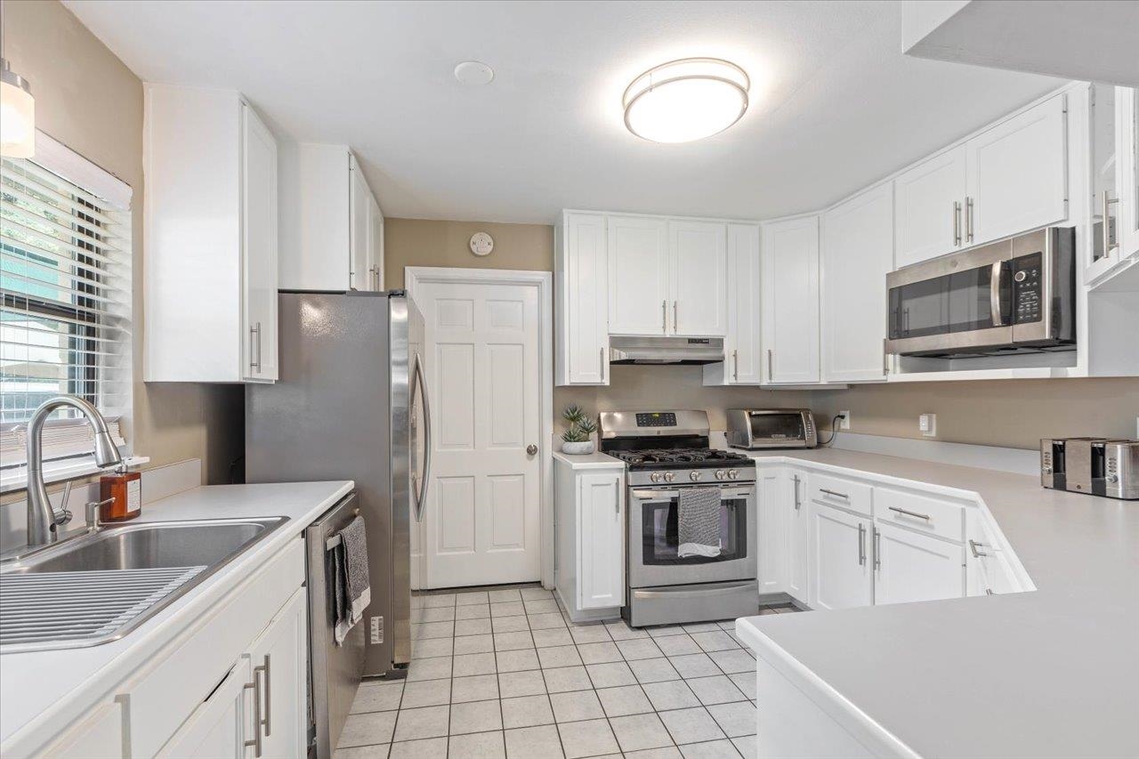 Kitchen with white cabinets, stainless steel appliances, and a double-basin sink beneath a window.