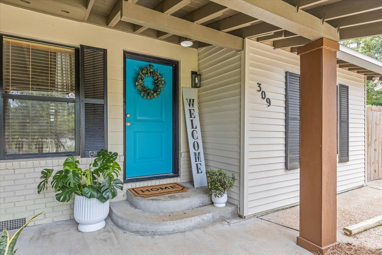 Home entry with a bright turquoise door, covered porch, and potted plants.