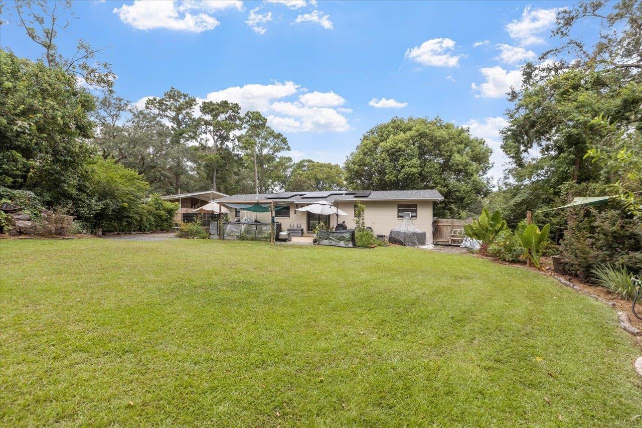 Single-story home beyond a broad lawn, with a covered patio, outdoor seating, and solar panels.