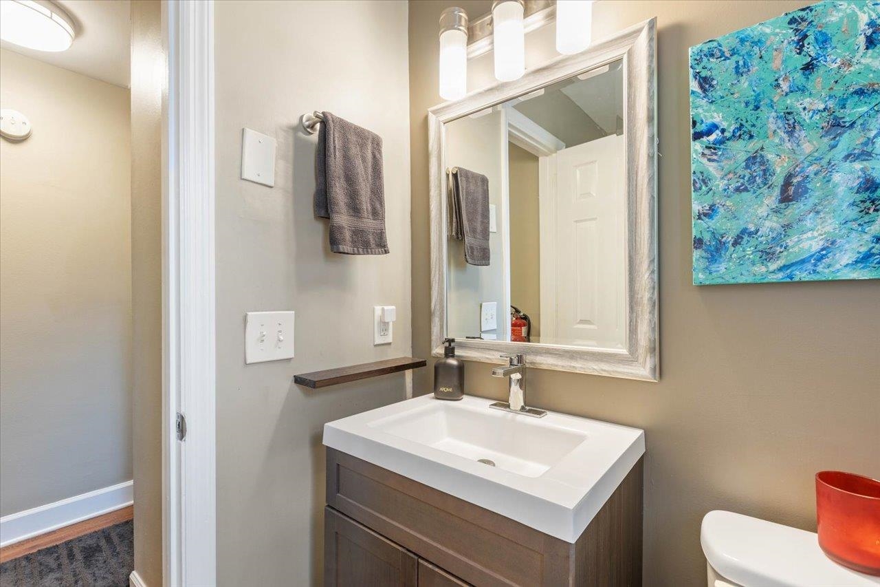 Bathroom vanity with a white sink, large framed mirror, gray towel, and blue abstract artwork.