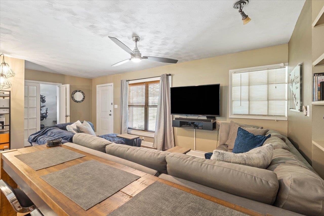 Living room with a large sectional sofa, wall-mounted television, ceiling fan, and wooden coffee table.
