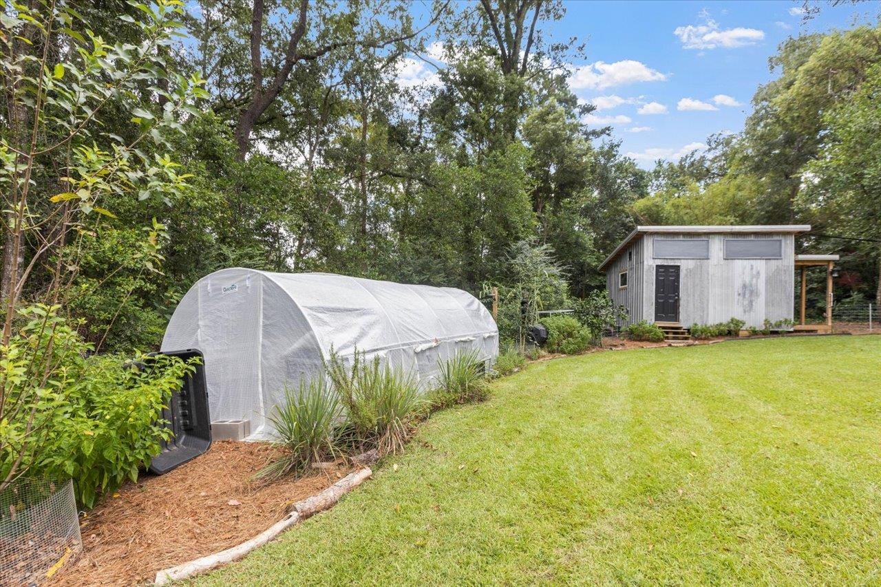 Backyard with a long white greenhouse, garden beds, and a small gray shed.