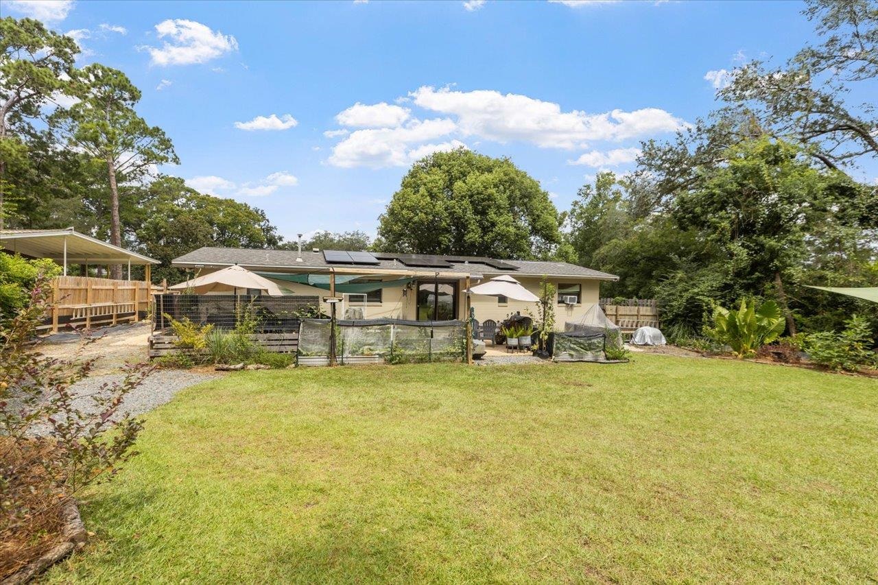 Single-story home with rooftop solar panels, a fenced patio, and a spacious lawn.